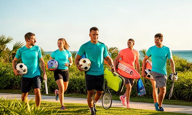 South Florida athletes carrying soccer, tennis, and water sports equipment beside a sunny coastal park